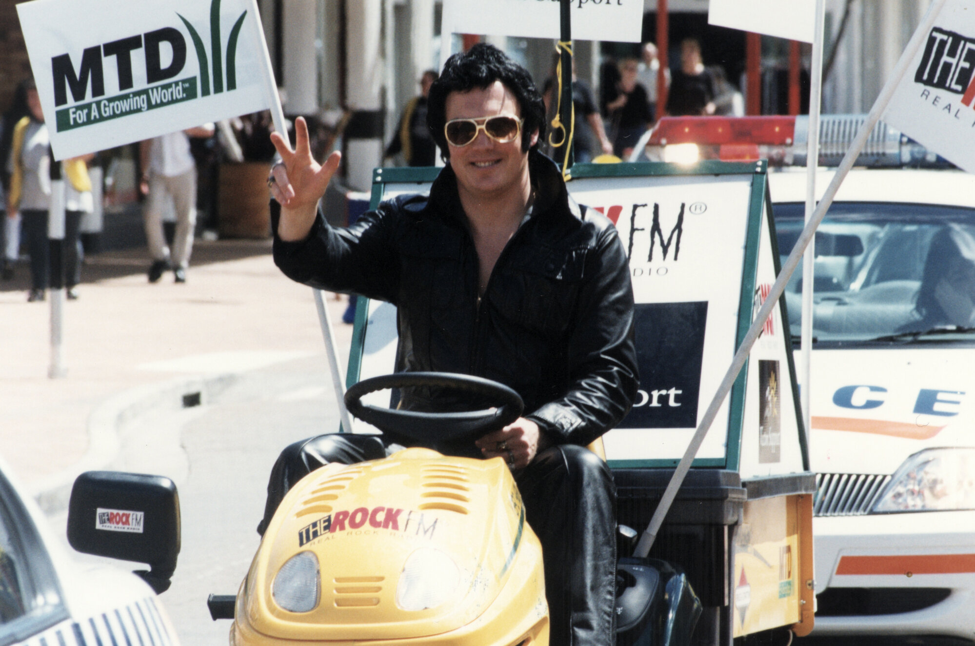 Victim Support fund-raiser; Constable Brian Childs drives ride-on mower up Main Street. 