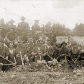 Soldiers with picks & shovels standing in trench.
