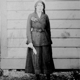 Woman; a Clifford? with plaited hair, wearing jacket, skirt, and white bonnet, and holding gloves.